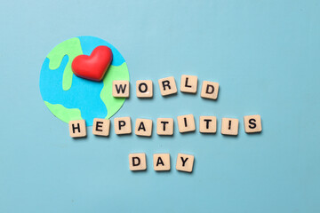 Fototapeta premium Top view of text WORLD HEPATITIS DAY on cubes and globe with a heart isolated on blue background