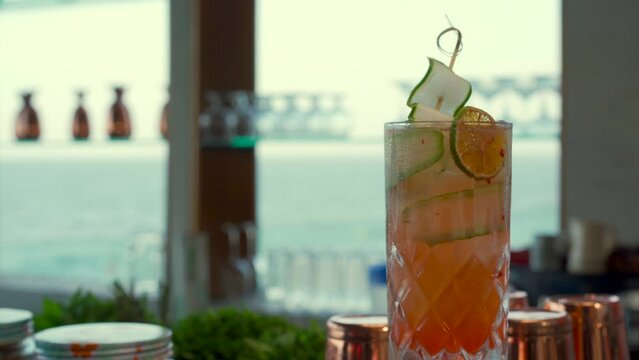Tequila sunrise mezcal cucumber an lemon garnish cocktail bayside bayfront fresh drink beach refresher  sea background blurry