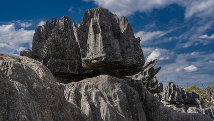 A bizarre black rock with sharp peaks against a background of blue sky and clouds. Steep folded...