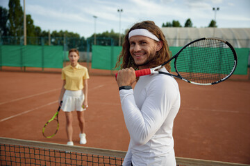Couple of friends playing tennis on court with focus on confident man