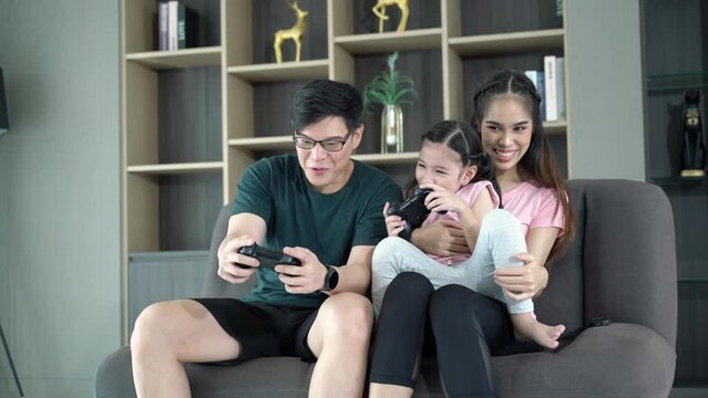 Happy girl playing video games with father and mother spending time together at home, parent people having activities with family