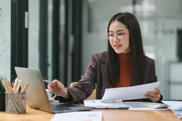 Happy smiling business woman working with laptop computer with paperwork at desk in a modern...