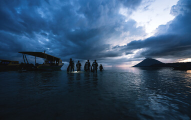 Divers walking into the ocean during sunset for a night dive in Bunaken, Sulawesi, Indonesia - obrazy, fototapety, plakaty