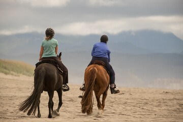 Horseback riding on ocean beach. Early in the morning two women riding together on horses at the...