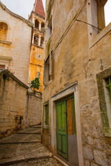 Fototapeta na wymiar A street of historic stone houses in Milna Village on Brac Island in Croatia with traditional kogule or kogulavanje paving. The bell tower of Church of Our Lady of the Annunciation is in background