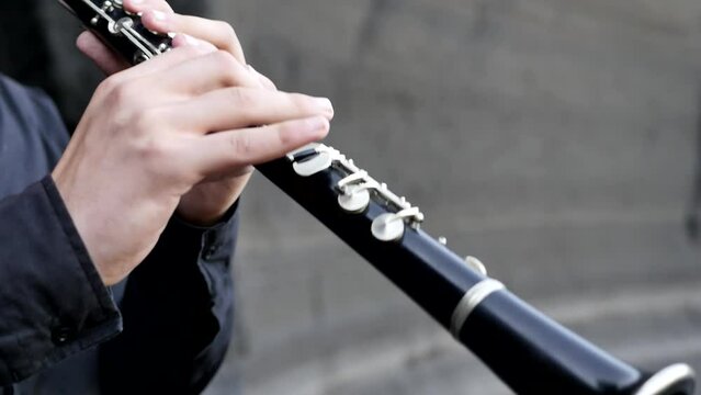 Close up of a teenager clarinetist playing the clarinet in the mountains. The guy standing among the rocks holds a clarinet and presses the keys with his fingers. Classical Middle Eastern Music