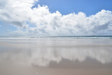 reflections of clouds in wet sand on a sunny beach
