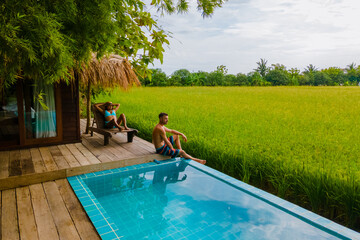 a couple of men and women in front of a Bamboo hut homestay farm, with Green rice paddy fields in...