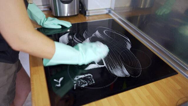 Woman scrubbing with soap and cloth an induction hob for cooking.