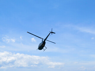 Black helicopter in flight. A small private helicopter against a blue sky and white clouds.