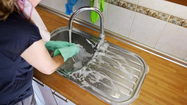 Woman scrubbing with scouring pad and soap a sink on the kitchen counter.