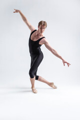 Fototapeta premium Sports Concepts and Ideas. Young Athletic Caucasian Ballet Dancer Man Posing in Stretching Pose With Hands Lifted in Line and Knees Bended in Black Tights On White.