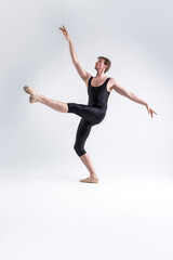 Fototapeta na wymiar Sports Ideas. Young Athletic Caucasian Ballet Dancer Man Posing in Dancing Stretching Pose With Hands Lifted Up in While Standing on Feet in Black Tights On White.