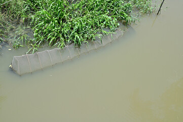 Closeup of Basket fish trap catch fishes in the canal with natural background at Thailand.