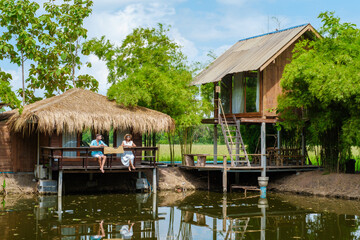 Fototapeta na wymiar Bamboo hut homestay farm with Green rice paddy fields in Central Thailand Suphanburi region, couple of men and women relaxing during a trip at the countryside of Thailand