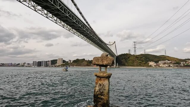 Old japanese rock lantern in the water in front of  Kanmon bridge and the kanmon strait in between the japanese island Honshu and Kyushu. Wabkari Shrine in Japan