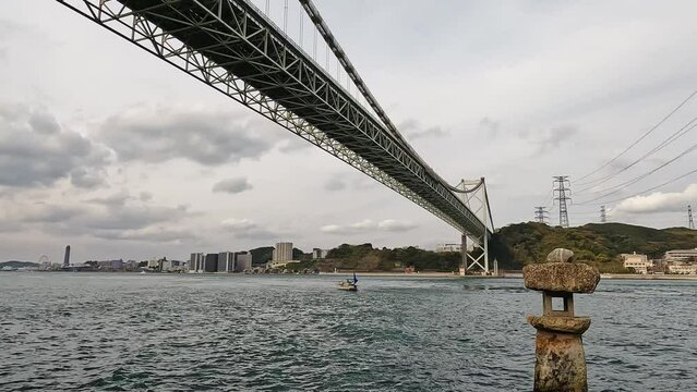 Old japanese rock lantern halfly submerged in water in  front of  Kanmon bridge and the kanmon strait in between the japanese island Honshu and Kyushu. View over the bridge and bay