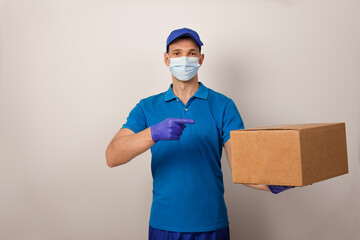 Obraz na płótnie Canvas Portrait of handsome attractive delivery man in a medical mask and gloves holding card-board box. Express delivery service. Copy space.