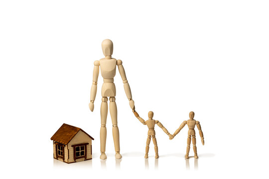 Concept image of a wooden mannequin adult with two children holding hands next to a small model house isolated on a white background with copy space.