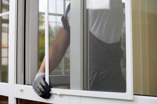 Close-up of the process of installing a mosquito net with the help of fasteners by a professional craftsman. Gloved worker inserts a white insect repellent grid into special brackets