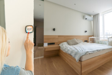 Smiling Indian woman using modern smart home system, controller on wall, positive attractive young...