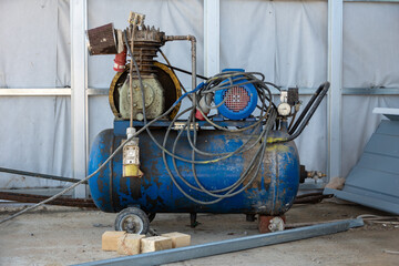 An old blue Working mobile air compressor for painting walls on a construction site. Engineering equipment