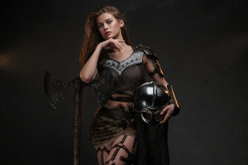 Beautiful Viking warrior model posing with a powerful axe and helmet showcasing strength and femininity in a medieval-inspired costume against a textured background