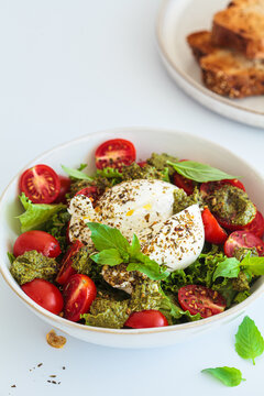 Burrata salad with cherry tomatoes, pesto and spices in bowl on white background.