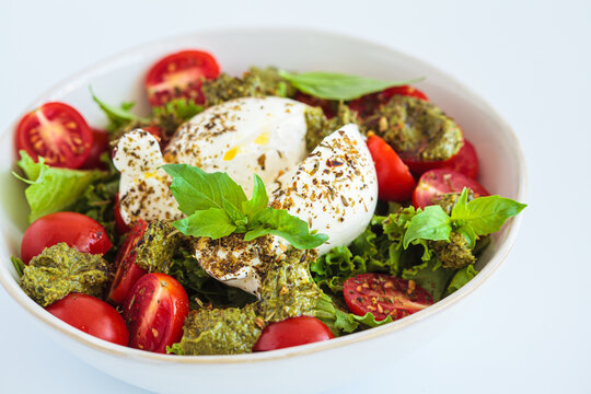 Burrata salad with cherry tomatoes, pesto and spices in bowl on white background.