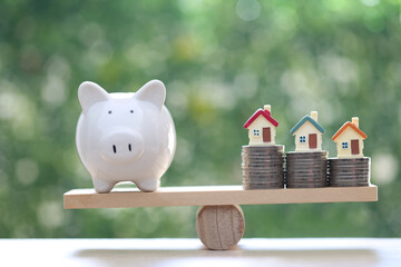 Interest rate up and Banking concept, Model house with piggy bank on wood scale seesaw on natural...