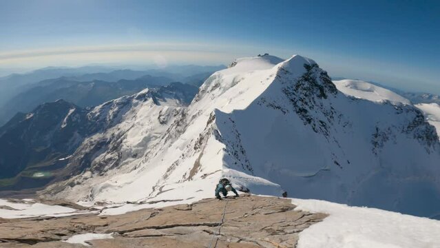 Mountaineer climbing a rock on high terrain with snowy alpine mountains in the background, with clear blue sky, during sunrise morning. Dufourspitze, Lyskamm, Monte Rosa, Switzerland