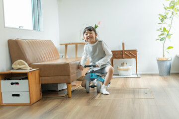 春の日中のあたたかい室内で三輪車に乗って笑顔で遊ぶ日本人の女の子