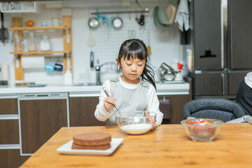 Fototapeta na wymiar 春の日中にキッチンで下を向いて生クリームの泡立てをする日本人の小学生の女の子