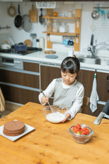 秋の昼間に自宅のキッチンでお菓子作り中に生クリームの泡立てに没頭する日本人の子ども