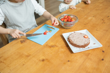 秋の日中に自宅のキッチンでお菓子作り中に苺を切るアジア人の子どもの手元