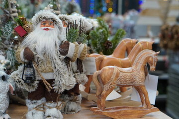 a figure of Santa Claus in a brown suit with a vintage lamp in his hands next to wooden horses on a shelf close-up in a supermarket