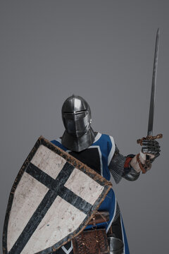 Medieval knight in active battle pose, wielding sword and shield against gray background