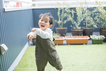 秋の日中の自宅のベランダで芝生の上で可愛く歌って踊る日本人の子供