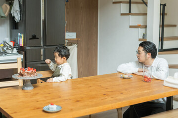 春の日中、台所でおやつのケーキを食べる日本人の男の子と見守る父親