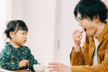 秋の朝、部屋でお菓子を食べるアジア人の男性と見守る小さな子ども