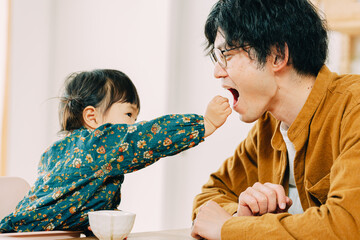 春の午後、部屋で口を開けて娘にお菓子を食べさせてもらう日本人の父親