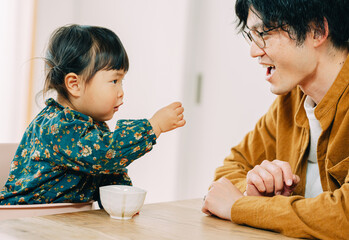秋の日中、室内で見つめ合って父親におやつをあげる日本人の幼い娘