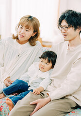 Obraz na płótnie Canvas 春の日中、家でソファに座って笑顔で前を見つめるアジア人の家族