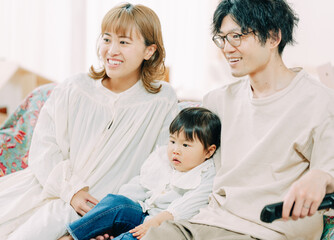 春の午後、家でソファに座り笑っている日本人の30代,夫婦と子ども