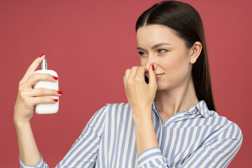 Dissatisfied woman with perfume bottle  in hand on pink background