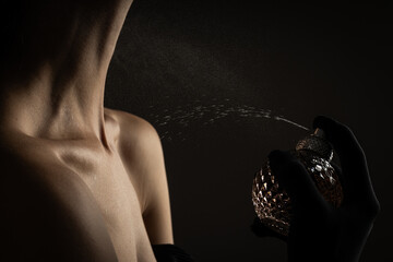 Young woman applying perfume on black background, close up