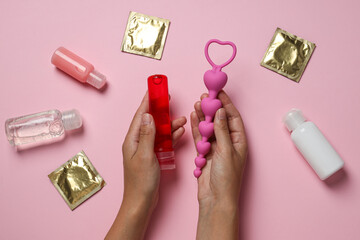 Lubricant with anal balls in hands on pink background with condoms