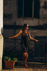 A young girl in the Italian patio at sunset in a low key. Little black dress with black glasses.