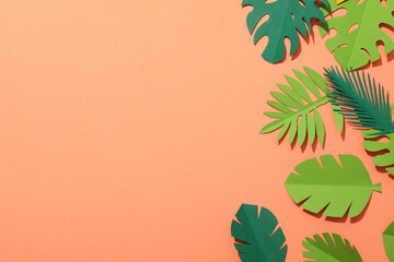 Paper green tropical leaves on a peach background.