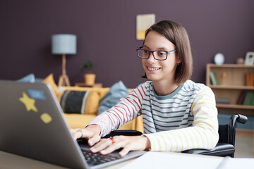 Portrait of smiling teenage girl with disability using laptop computer at home, copy space